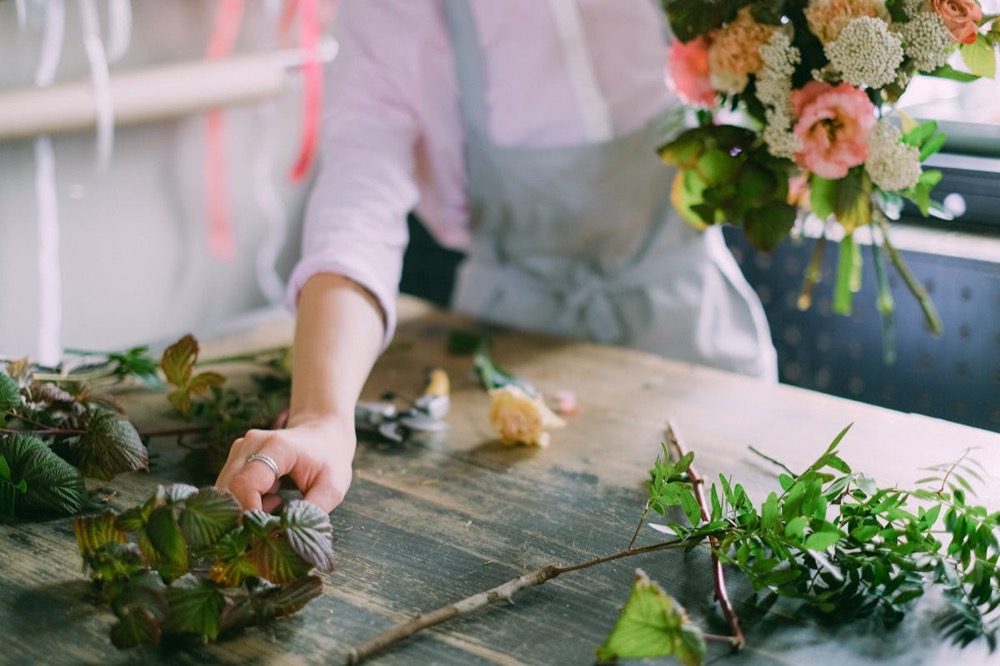 Studio hands trimming stems at a wooden workbench, surrounded by seasonal blooms for a custom install